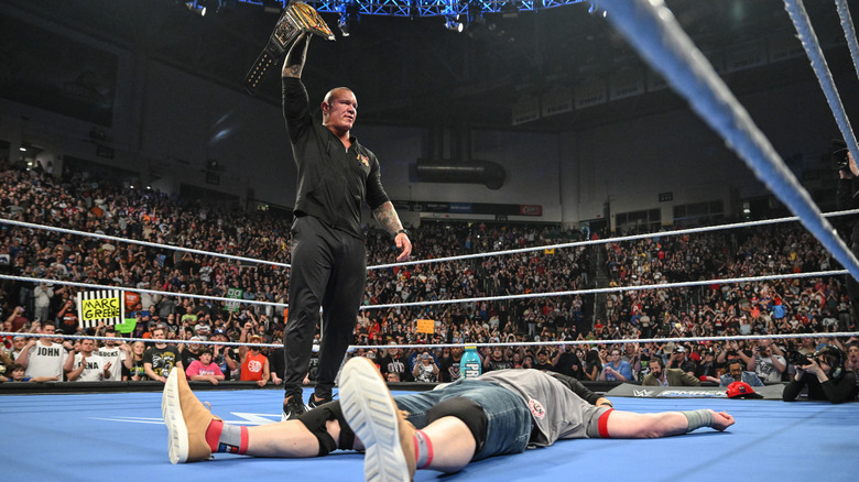 Randy Orton stands over John Cena in the ring, holding up title belt