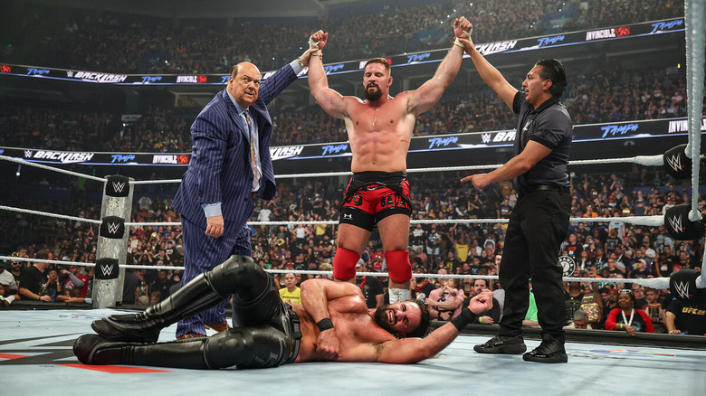 Bron Breakker stands victorious over Seth Rollins, Paul Heyman and the referee raising his arms, at WWE Backlash