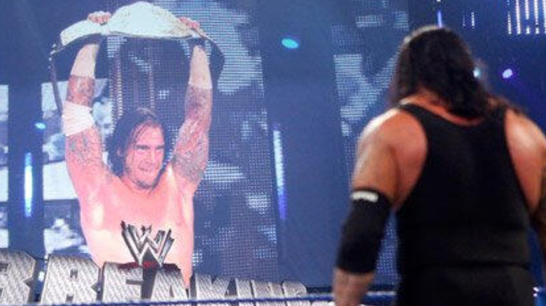 CM Punk holding up the WWE World Heavyweight Championship as The Undertaker looks up