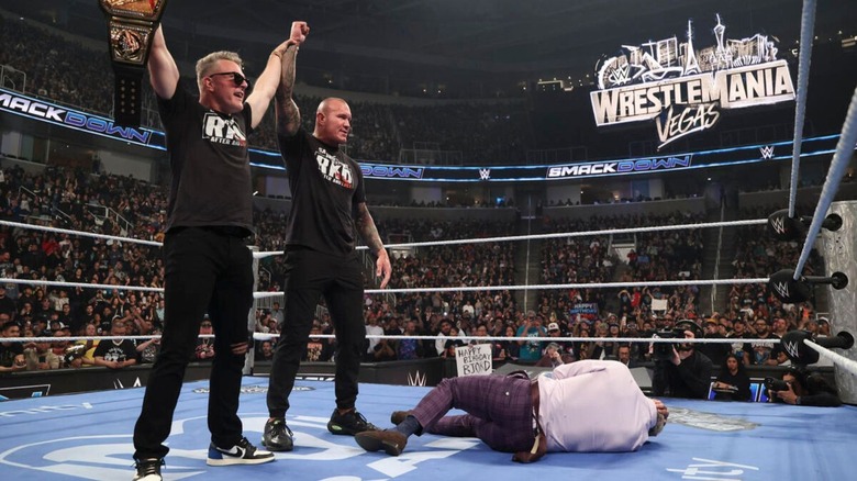 Pat McAfee holds up the Undisputed WWE Championship alongside Randy Orton, as they stand over a fallen Cody Rhodes, in the ring during an episode of "WWE SmackDown."