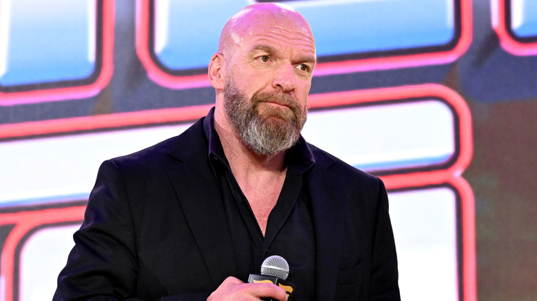 Paul Levesque in a black suit holding a mic