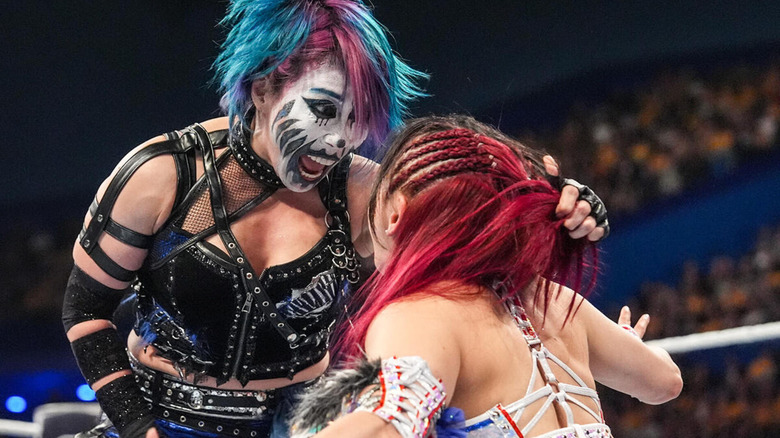 Asuka grabs the back of IYO SKY's head and shouts at her.