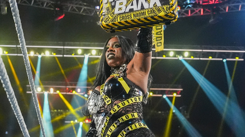 WWE star Naomi holds the Money In the Bank briefcase over her head while standing in the ring