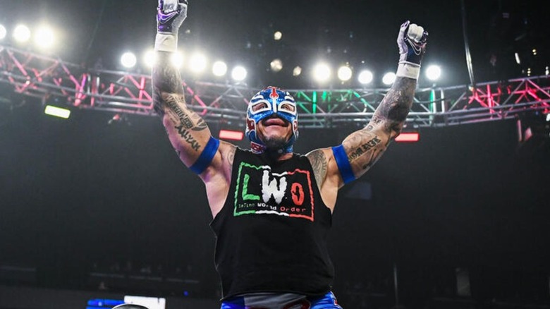 Rey Mysterio poses for the crowd on the turnbuckle before a match, wearing an LWO shirt, on an episode of WWE programming.