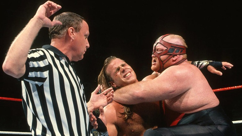 Vader locking Shawn Michaels into a Submission hold while referee Earl Hebner presides.