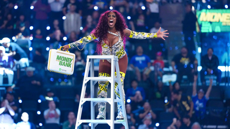 Naomi poses on a ladder while holding the women's Money in the Bank briefcase.