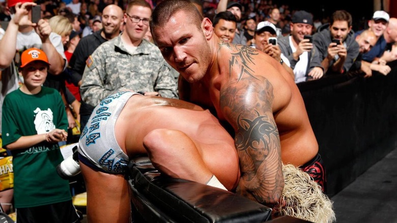 Randy Orton sets up Dolph Ziggler for his signature draping DDT over the ring barricade.