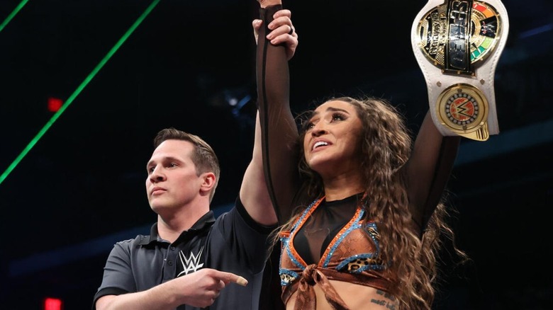 A referee holds up the arm of Wren Sinclair, as she holds up her newly-won WWE Women's Speed Championship.
