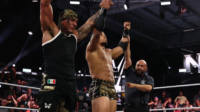 A referee raises the hand of Lucien Price, who holds up Bronco Nima's, after a victory on "WWE NXT."