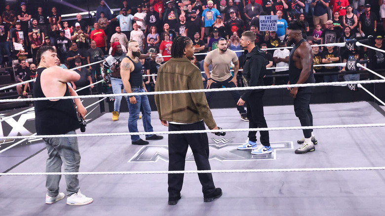 Grayson Waller in the ring surrounded by Mason rook, Saquon Sugars, Tony D'Angelo, EK Prosper, Cruz Montana, and Keanu Carver on "WWE NXT"