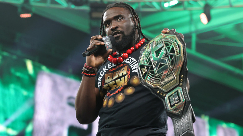Oba Femi speaking into a mic while holding the WWE NXT Championship