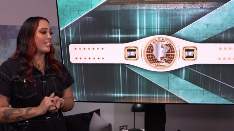 Ava Raine stands in front of a display of the new "NXT" Women's North American Championship.