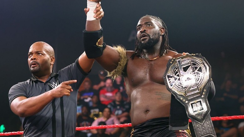 Oba Femi has his hand raised as he holds his "NXT" Championship.