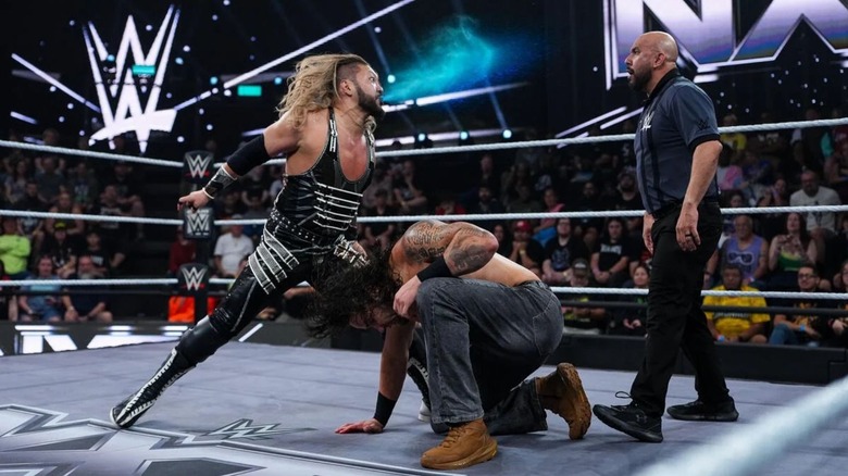 Naraku spits blue mist in the face of a referee, as Shiloh Hill ducks in the ring, during an early October 2026 match on "WWE NXT."