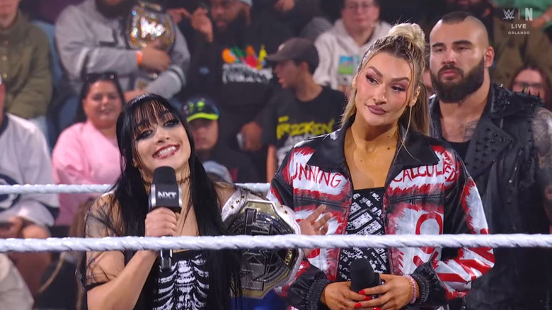 Paxley speaking on the microphone as Dame looks at her