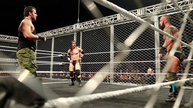 Roderick Strong, Adam Cole, and Eric Young in the ring surrounded by a WarGames cage