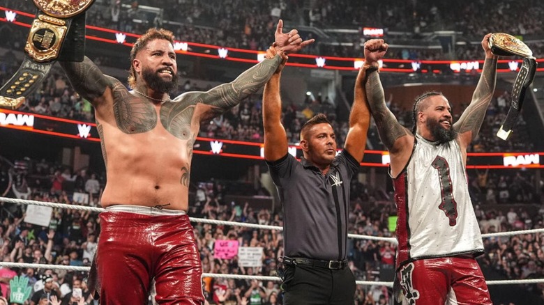 A referee holds up The Uso's arms in victory, alongside the WWE World Tag Team Championships, after their victory on an episode of 