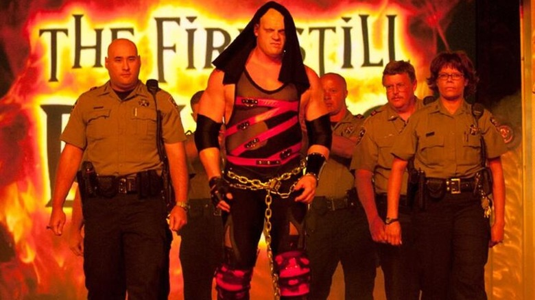 Kane chained up walking to the ring with police shortly after his run after losing his mask, 2003.