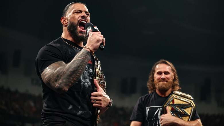 Roman Reigns yells into a microphone as Sami Zayn watches on "WWE Raw"