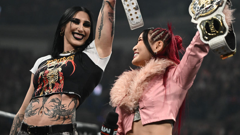 Rhea Ripley and IYO SKY smile at each other as they hoist up the WWE Women's Tag Team Championships.