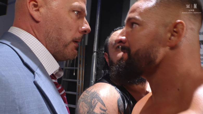 Spit dribbles from an irate Adam Pearce's chin as he heatedly stares at Bron Breakker, who is being held back by Bronson Reed.