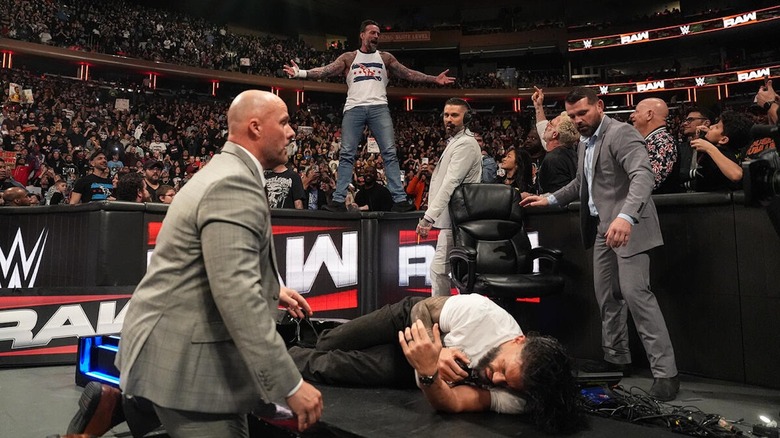 CM Punk poses above Roman Reigns, lying in the wreckage of the announce table, on "WWE Raw"