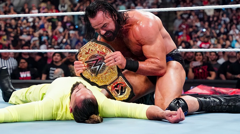 Drew McIntyre holds world title beelt over a fallen Seth Rollins