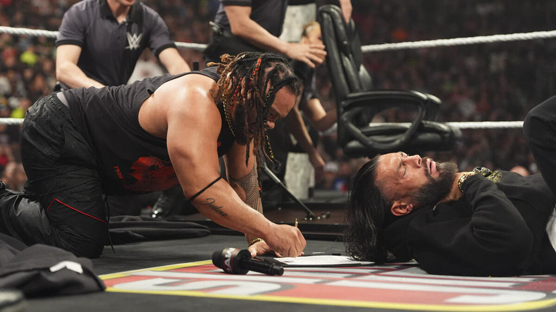Jacob Fatu signs a contract in the ring while Roman Reigns struggles to breathe beside him on "WWE Raw"