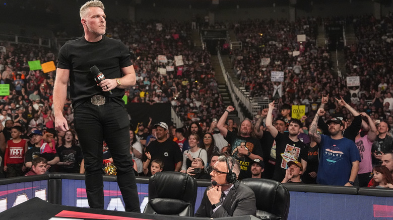 Pat McAfee standing on the commentary desk with a mic