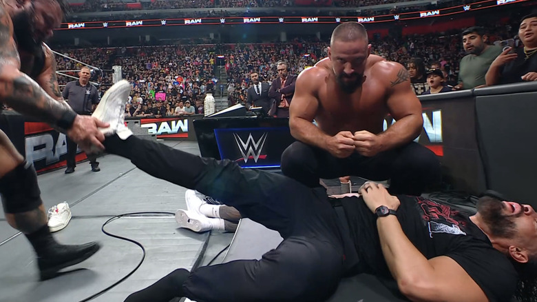 Bronson Reed de-shoes a prone Roman Reigns as Bron Breakker stares directly into the camera.