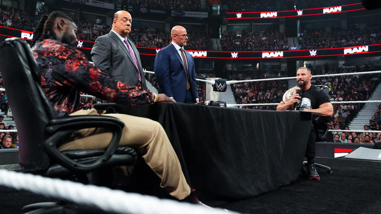 Bron Breakker and Oba Femi sitting at a table in the ring while Paul Heyman and Adam Pearce stand beside it on "WWE Raw"