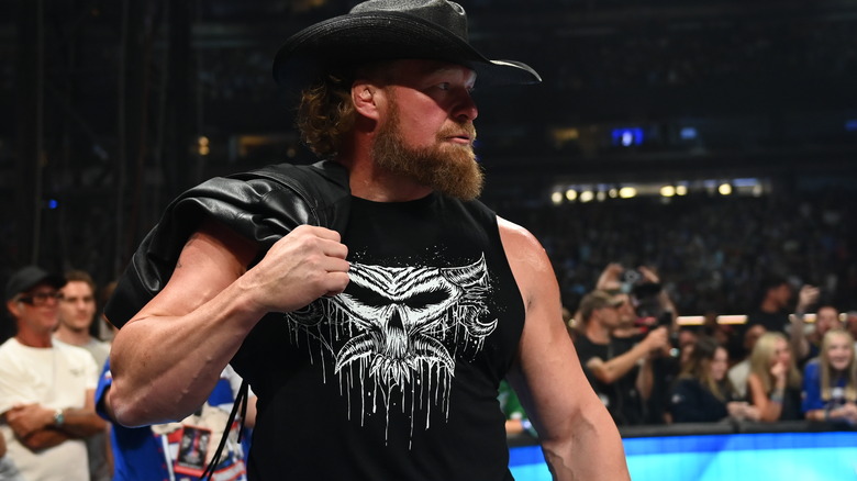 Brock Lesnar looks off to the side as he dons a cowboy hat and a leather jacket over his shoulder.
