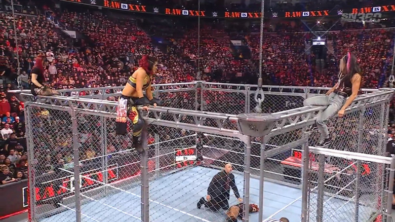 Damage CTRL on top of the cage as Lynch lays in the ring