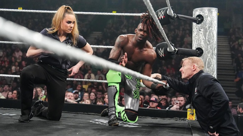 WWE star Je'Von Evans kneels in the corner of the ring next to the referee of his match and someone from the medical team after the referee called for stoppage to his match due to concerns of a head injury