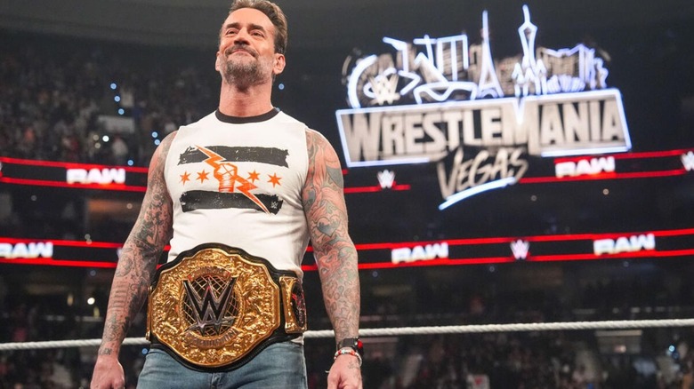 CM Punk smirks up the ramp toward Roman Reigns, the WrestleMania sign looming behind him, on an episode of 