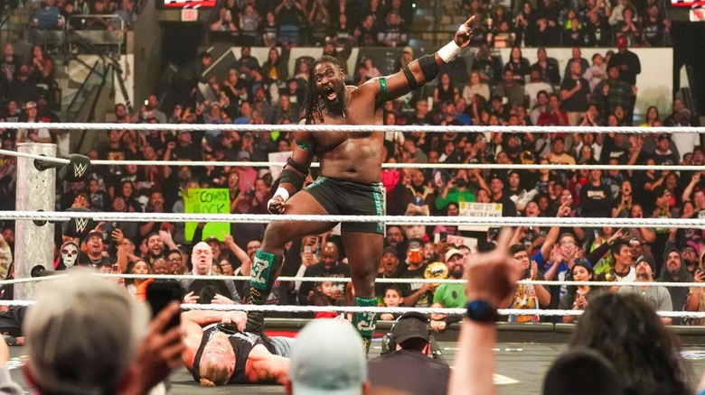 Oba Femi stands in the ring, one foot on Brock Lesnar, pointing at the WrestleMania sign during an episode of 