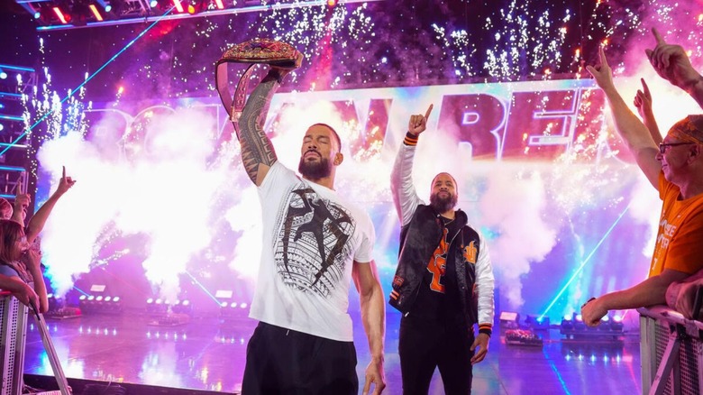 World Heavyweight Champion Roman Reigns, flanked by Jimmy Uso, holds up the title as he heads down the ramp to the ring during a segment on 