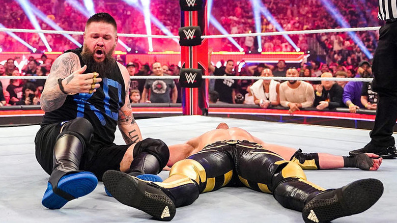 Kevin Owens looks at brass knuckles while next to a fallen Logan Paul