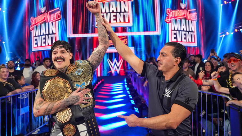 Dominik Mysterio holds his AAA Mega Championship and Intercontinental Championship titles with one hand, and his other is raised by the referee on the entrance ramp.