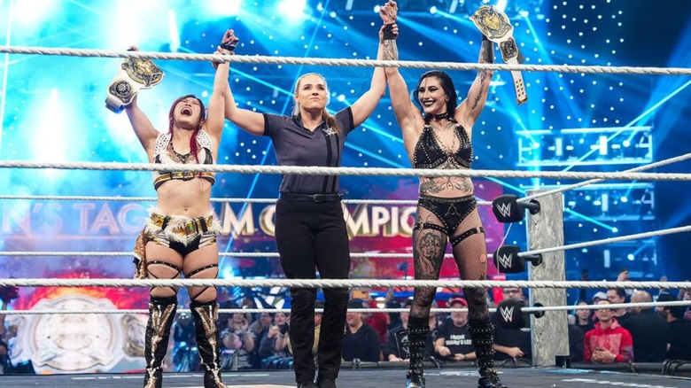 Referee Jessika Car holds up IYO SKY and Rhea Ripley's hands, as they hoist the WWE Women's Tag Team Championships after winning the belts on WWE Raw.