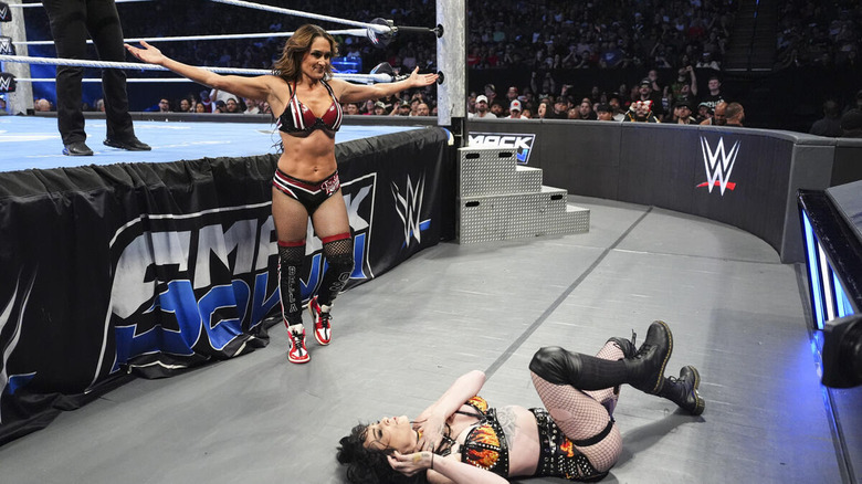 Nikki Bella poses over a fallen Paige outside the ring on "WWE SmackDown"