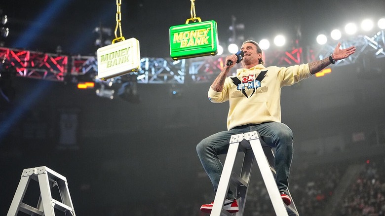 CM Punk sits on a ladder while speaking into a microphone on 