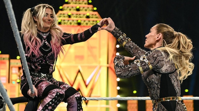 Charlotte Flair and Alexa Bliss hit a heart hands pose, with Bliss sitting on the top turnbuckle, during the opening of the 2026 Women's Royal Rumble.