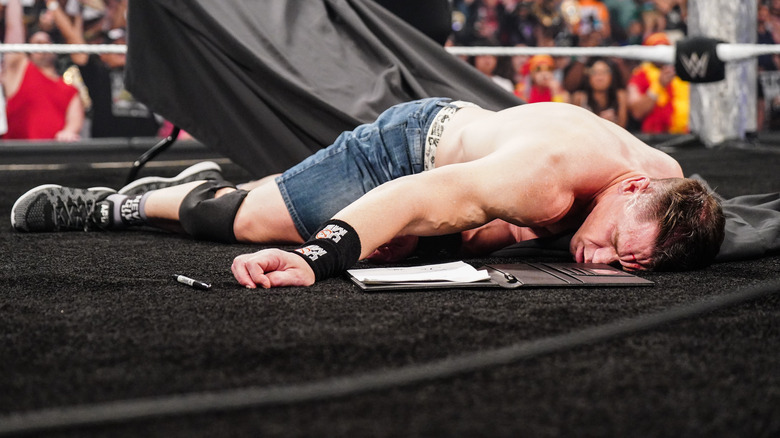John Cena lies senseless in the ring amidst the wreckage of a table beside his WWE SummerSlam contract on 