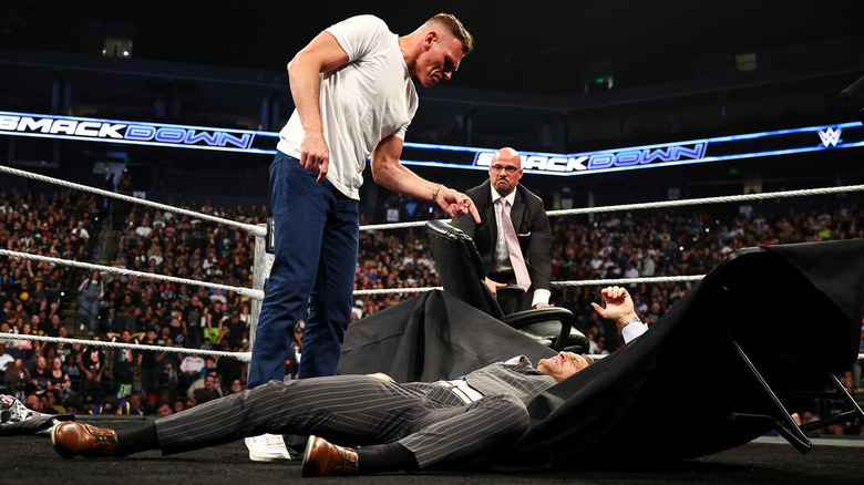 GUNTHER points down at a fallen Nick Aldis, lying in the wreckage of a table on "WWE SmackDown" as Adam Pearce looks on