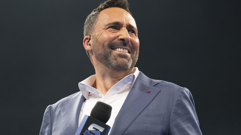 Joe Tessitore smiles as he holds a "WWE SmackDown" microphone.