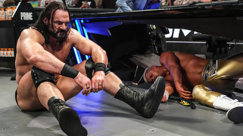Drew McIntyre sits next to a destroyed Cody Rhodes after kicking him through the announce table.