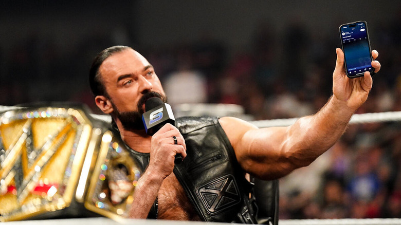 Drew McIntyre holds up his phone while speaking into a microphone on "WWE SmackDown"