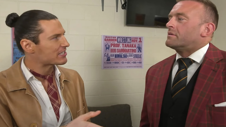 Kit Wilson, in a tan suit and red tie, complains to Nick Aldis.