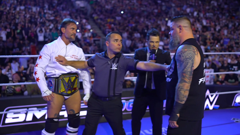 Punk and Owens staring down one another during the ring announcement as the referee holds them both back